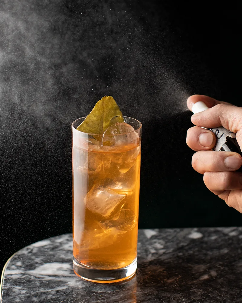 Cocktail in a highball glass with leaf garnish and spray at Graali Bar