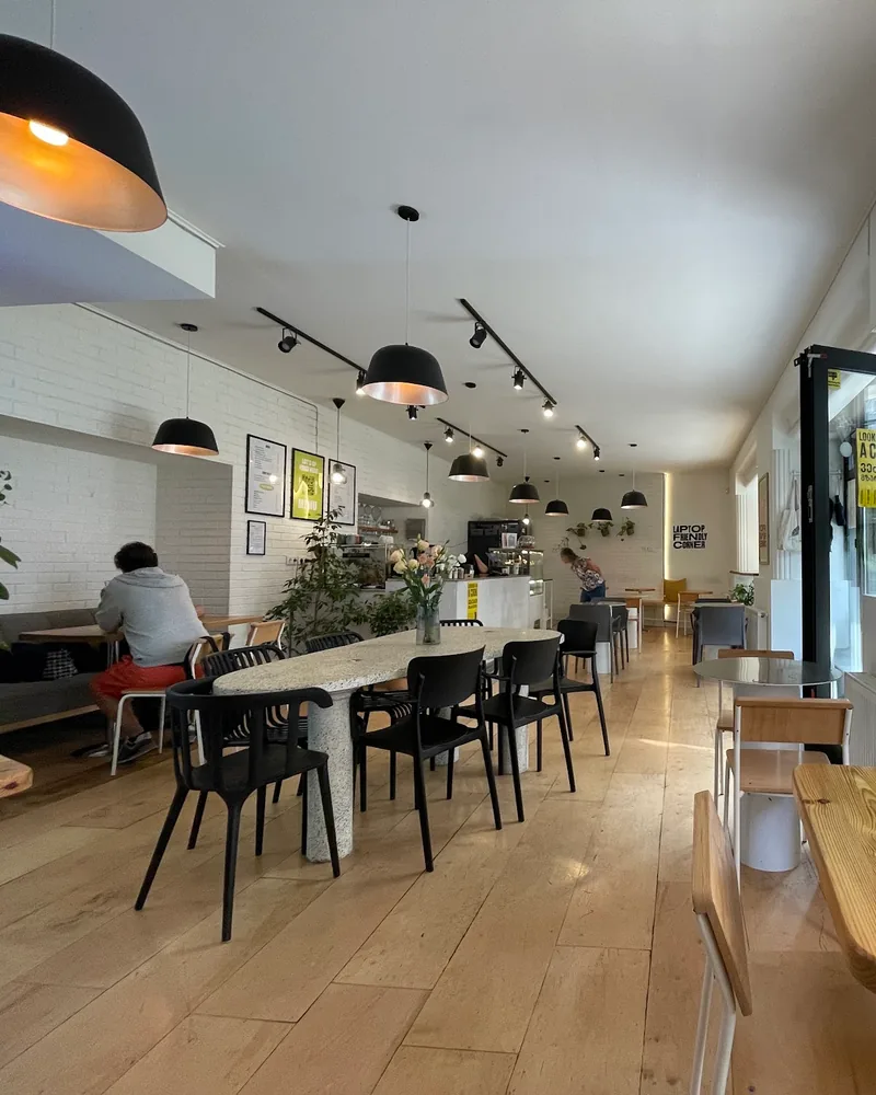 Bright cafe dining room with a long terrazzo table and black pendant lights at HURMA