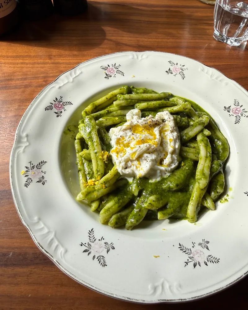 Green pesto pasta topped with stracciatella on a floral vintage plate at Italian Pasta