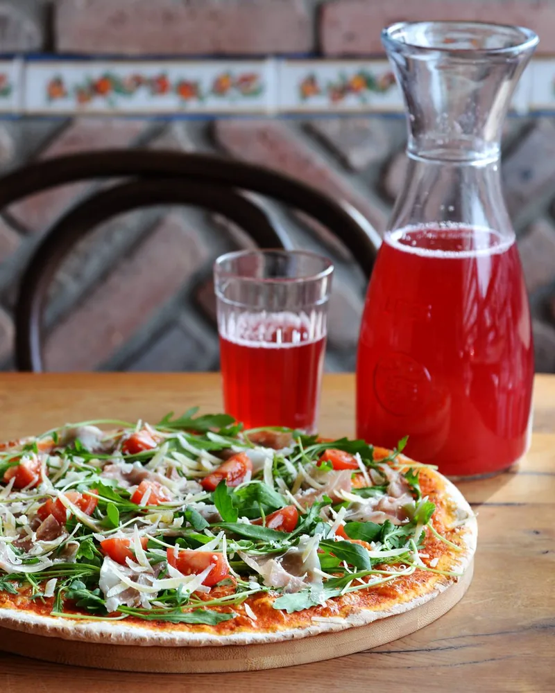 Arugula and prosciutto pizza with a carafe of red berry compote at Kakhelebi