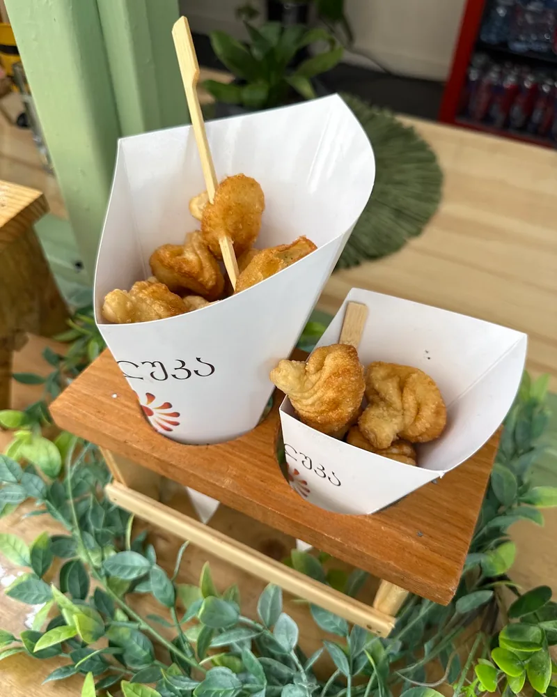 Fried mini khinkali in paper cones on a wooden stand at Khinkluka
