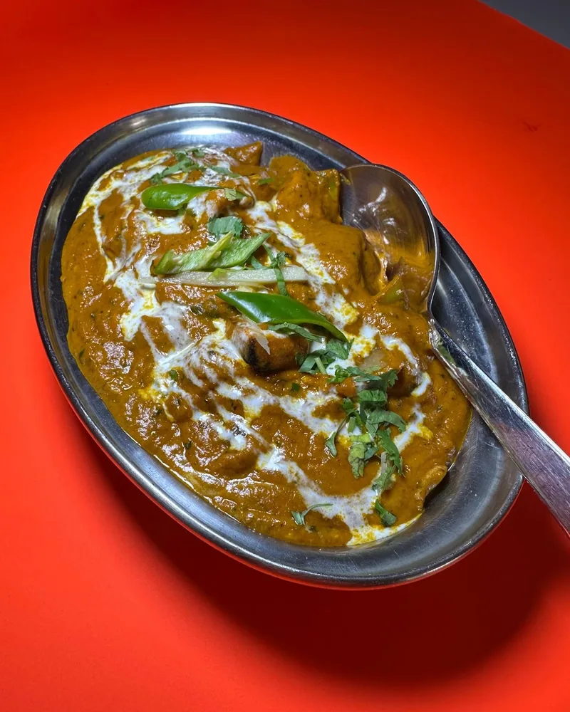 Indian curry in an oval metal dish with a spoon at Khushi Indian Restaurant