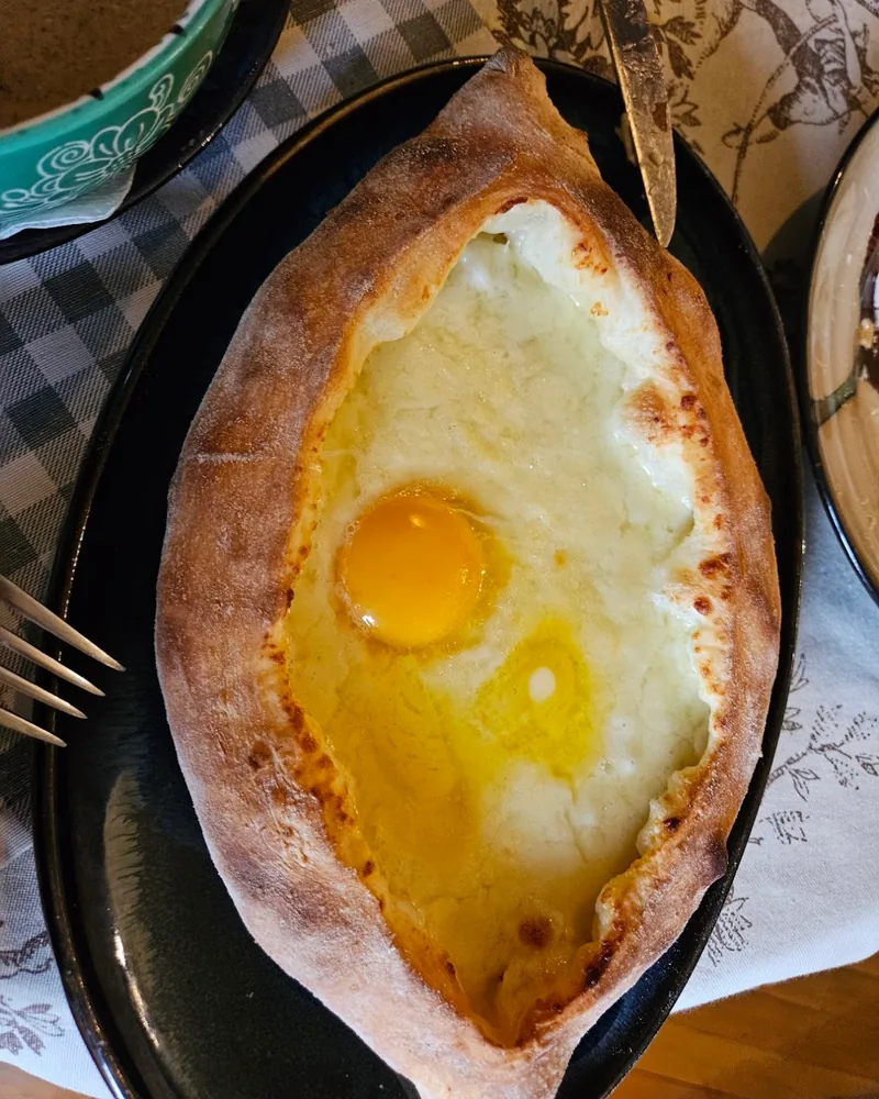 Adjarian khachapuri on a black oval plate at Kneina