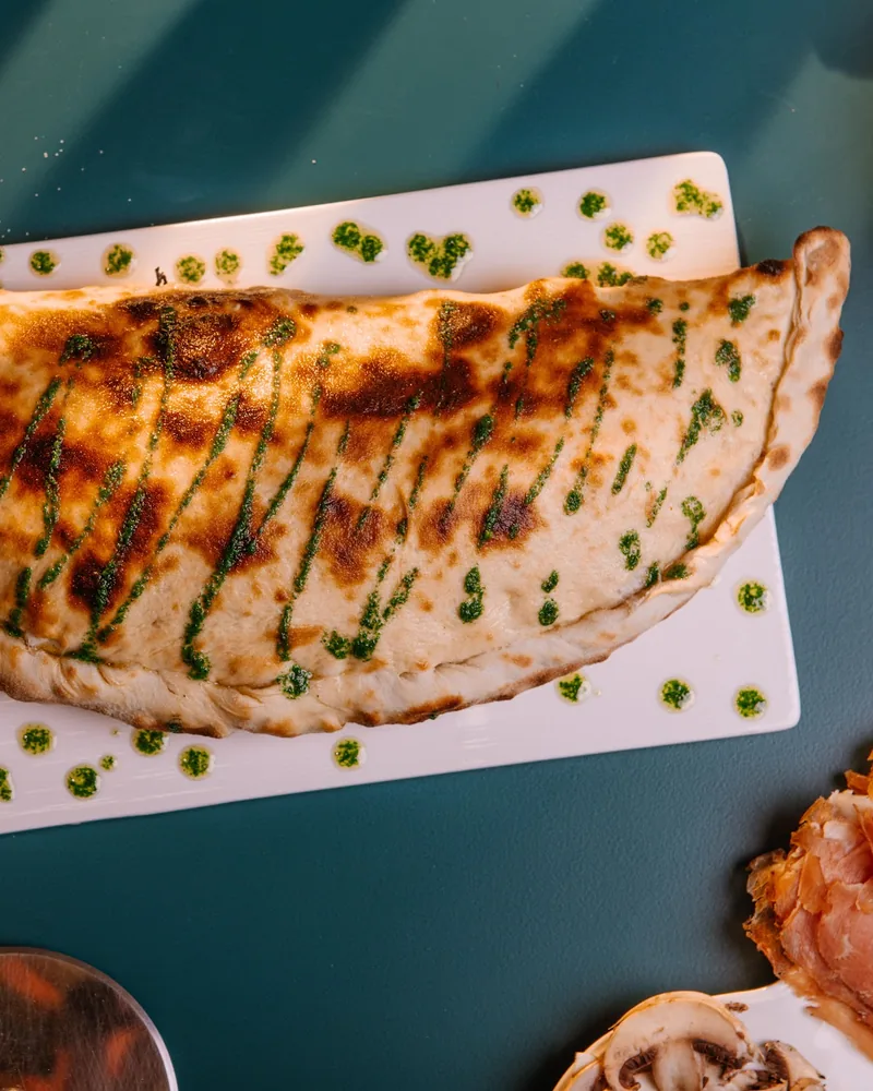 Calzone on a rectangular plate drizzled with pesto at La Crosta Pizzeria