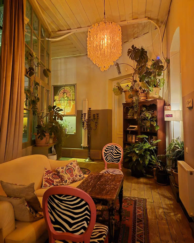A high-ceilinged room with zebra-print chairs, a cream sofa, potted plants and a chandelier made of shell discs
