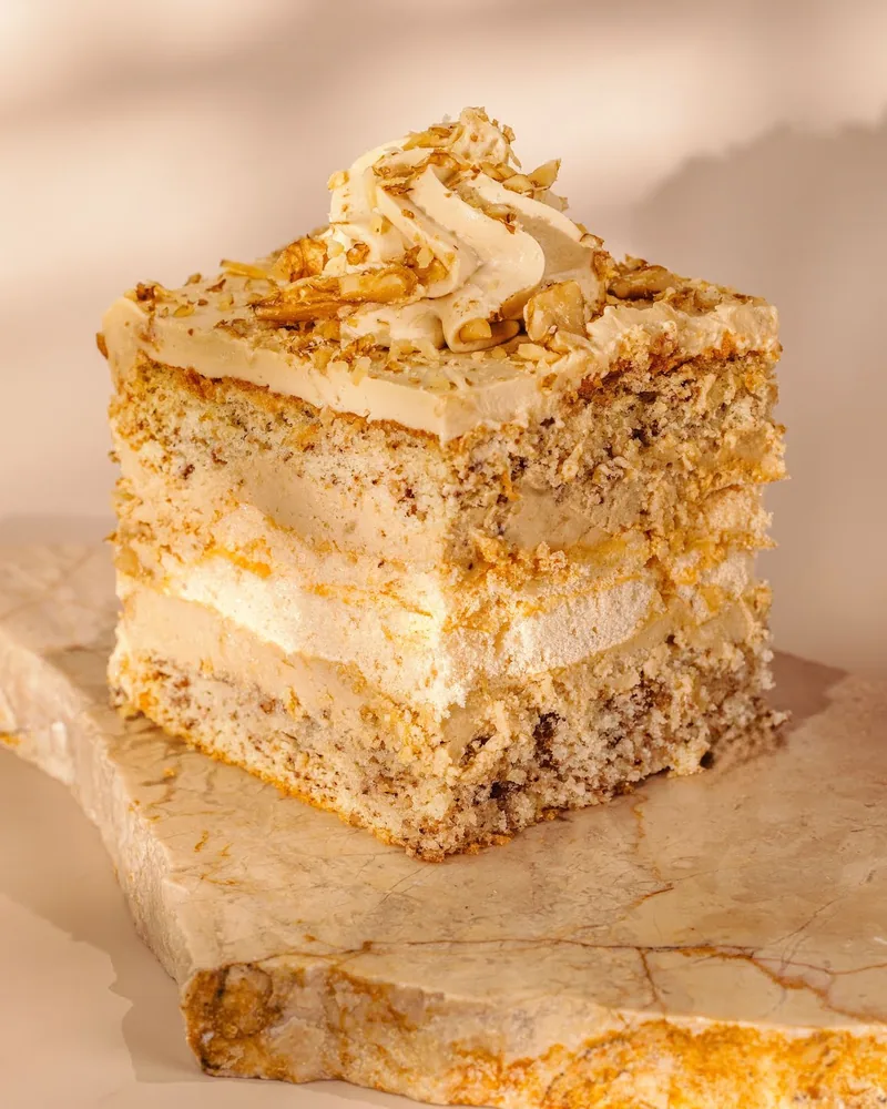 Slice of layered walnut cake on a stone slab at Lika