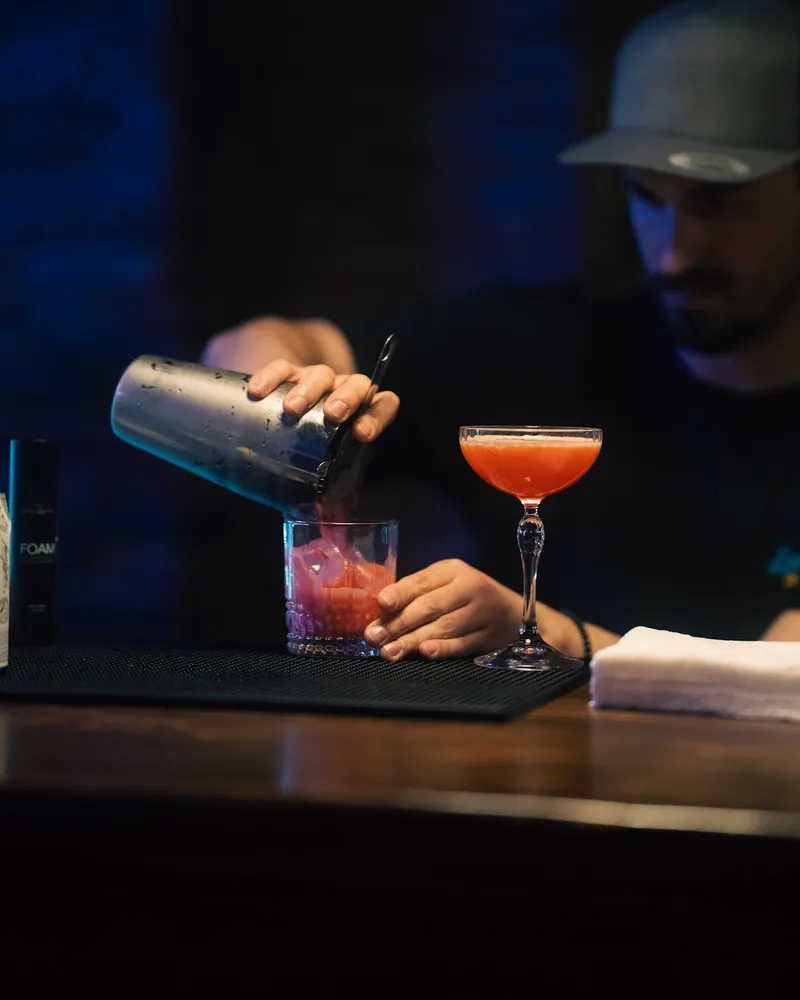 Bartender pouring a pink cocktail into a rocks glass at Looper's Bar