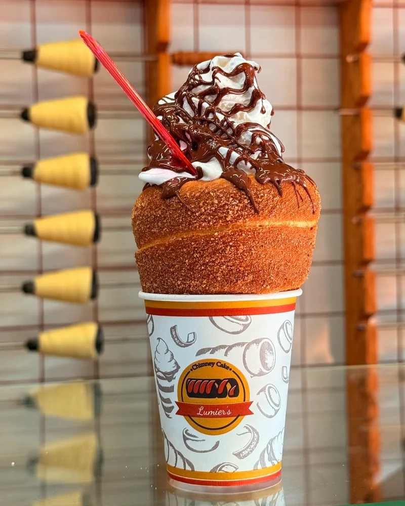 Chimney cake in a cup topped with whipped cream and chocolate syrup at Lumier’s Chimney Cake