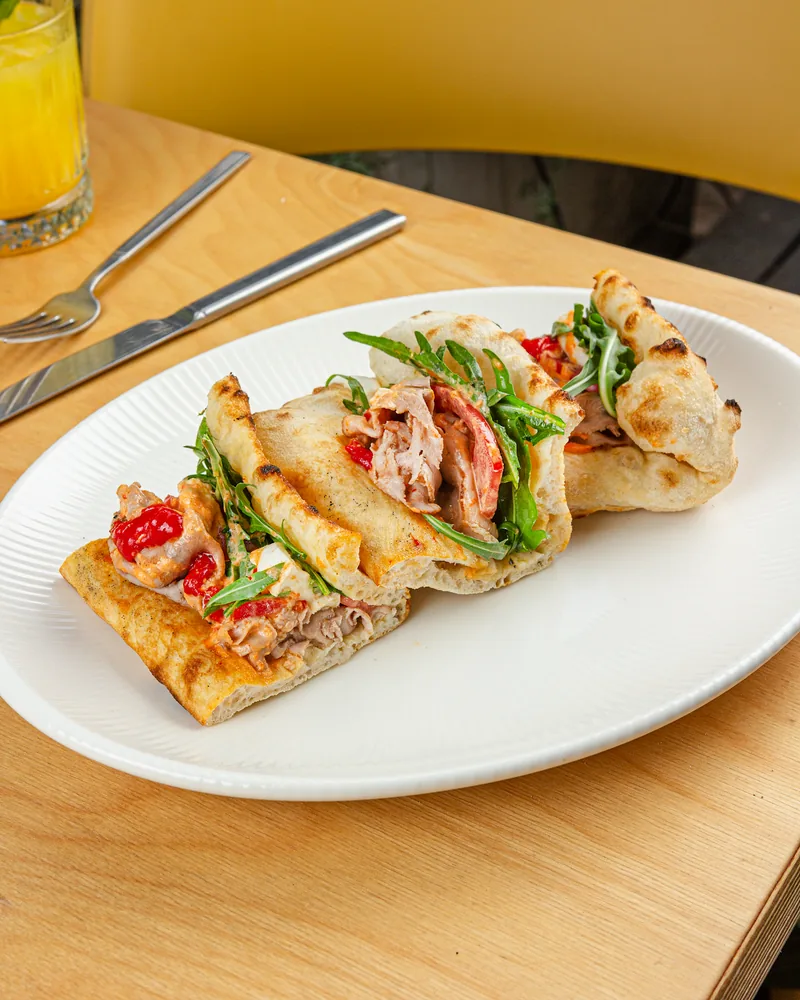 Sliced panuozzo sandwich filled with meat and arugula on an oval plate at Luna Pizza Bar