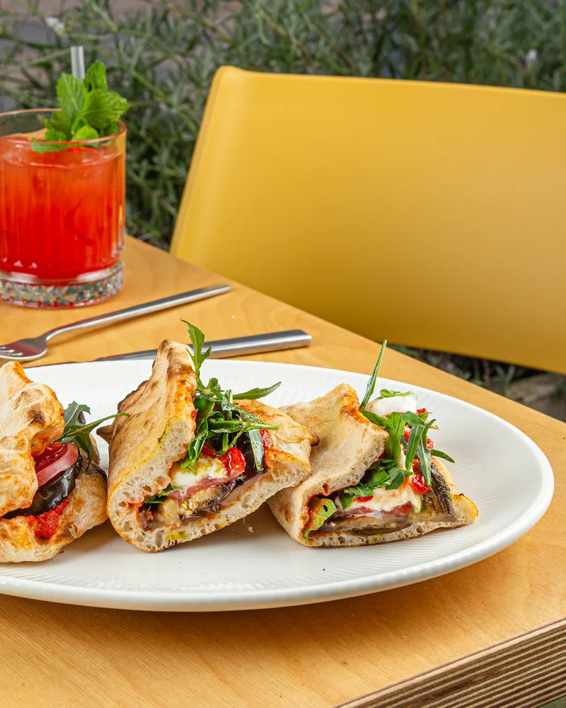 Panini sandwiches on a white plate with cocktail behind at Luna Pizza Bar