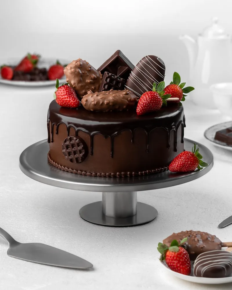 Chocolate drip cake with strawberries and chocolate bars on a stand at Madart