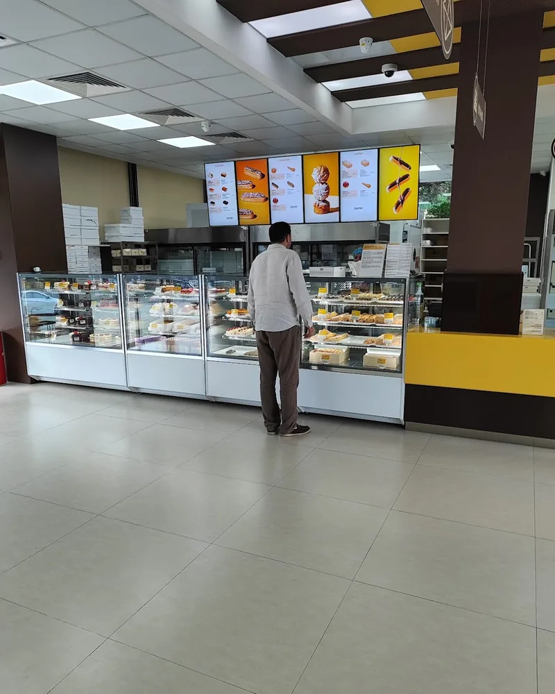 Bakery display counter with pastries and a customer at Madart