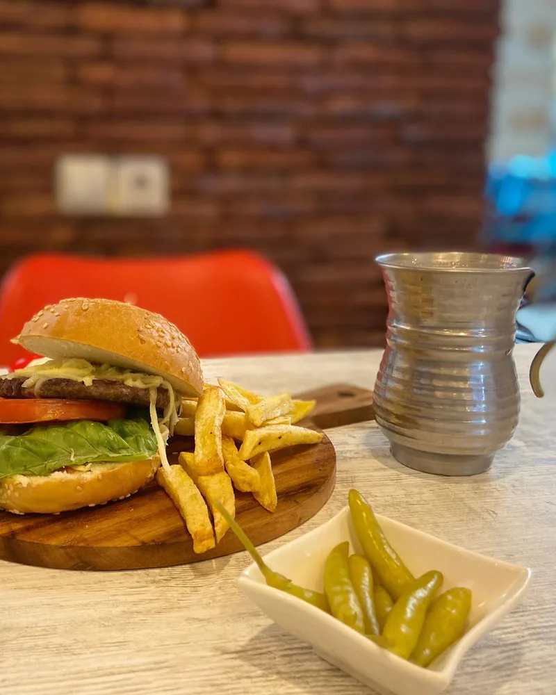 Cheeseburger with French fries on a wooden board and metal mug at Magical Shawarma