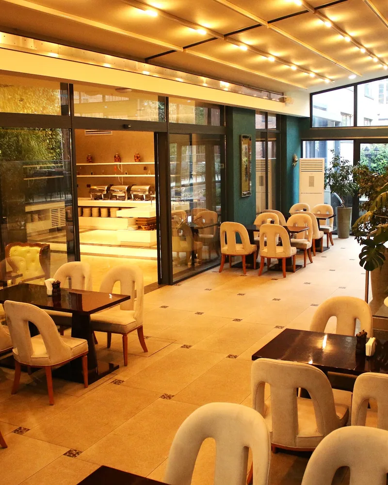 Glass-enclosed indoor dining area with cream chairs at Maharajah Lounge