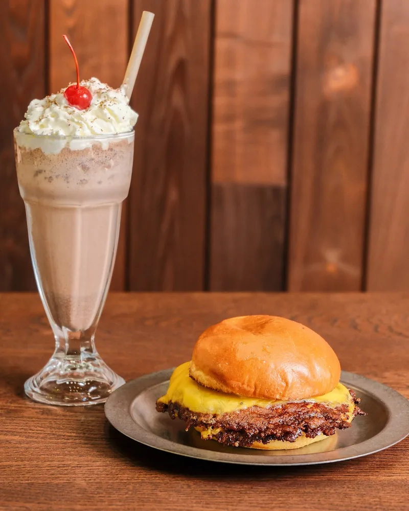Cheeseburger on a metal plate next to a chocolate milkshake at Melting Pot