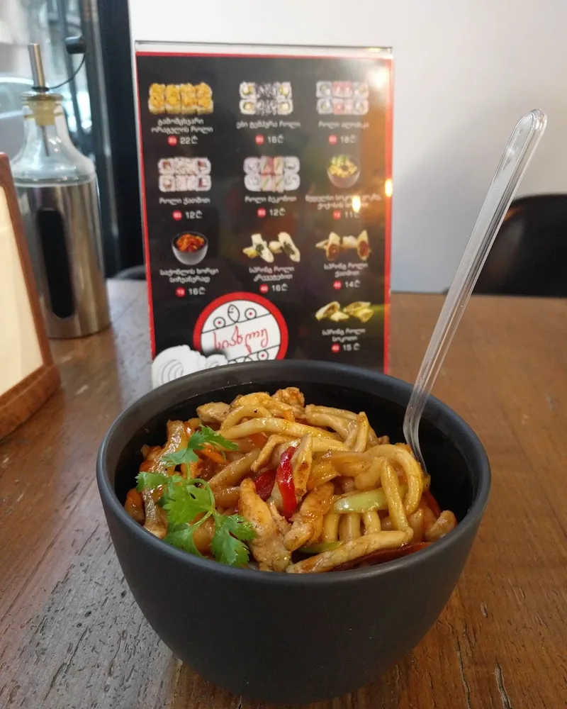 Stir-fried noodles with chicken in a black bowl at Mochi