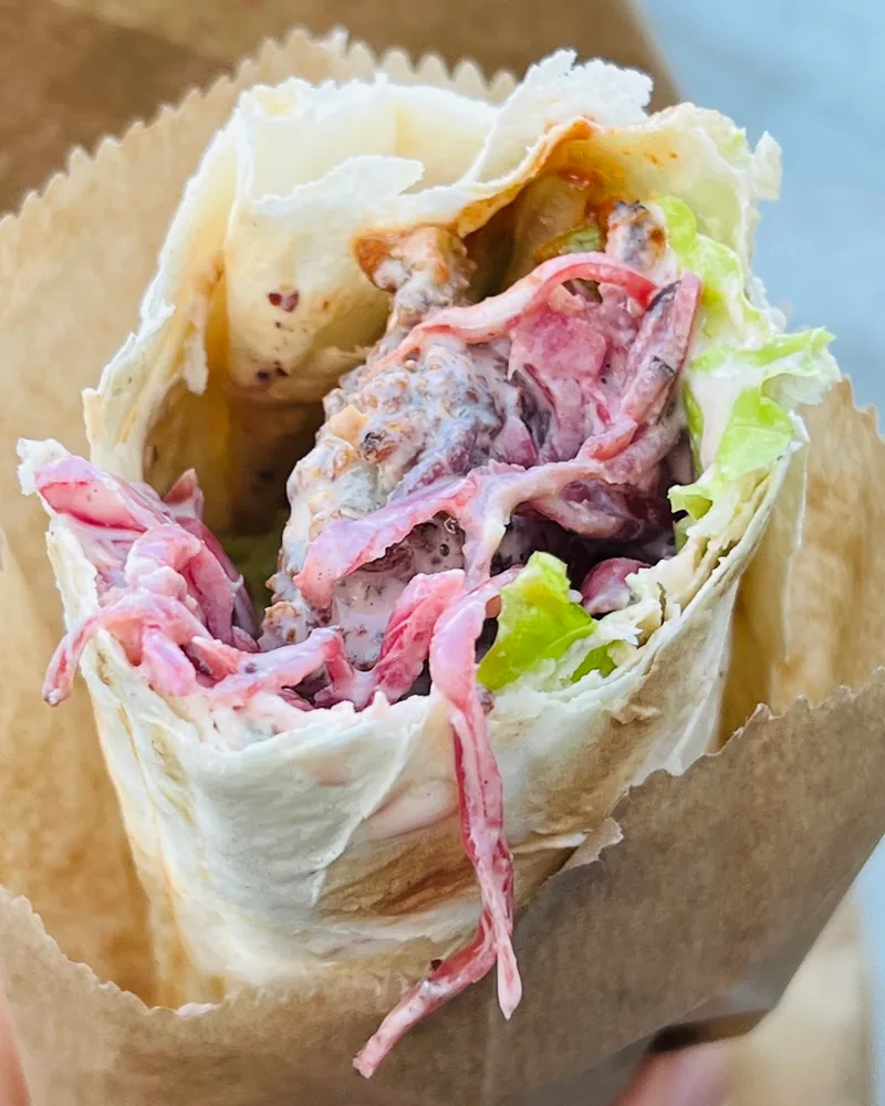 Falafel wrap with lettuce, pickled red cabbage and tahini sauce in a paper sleeve at Muhudo