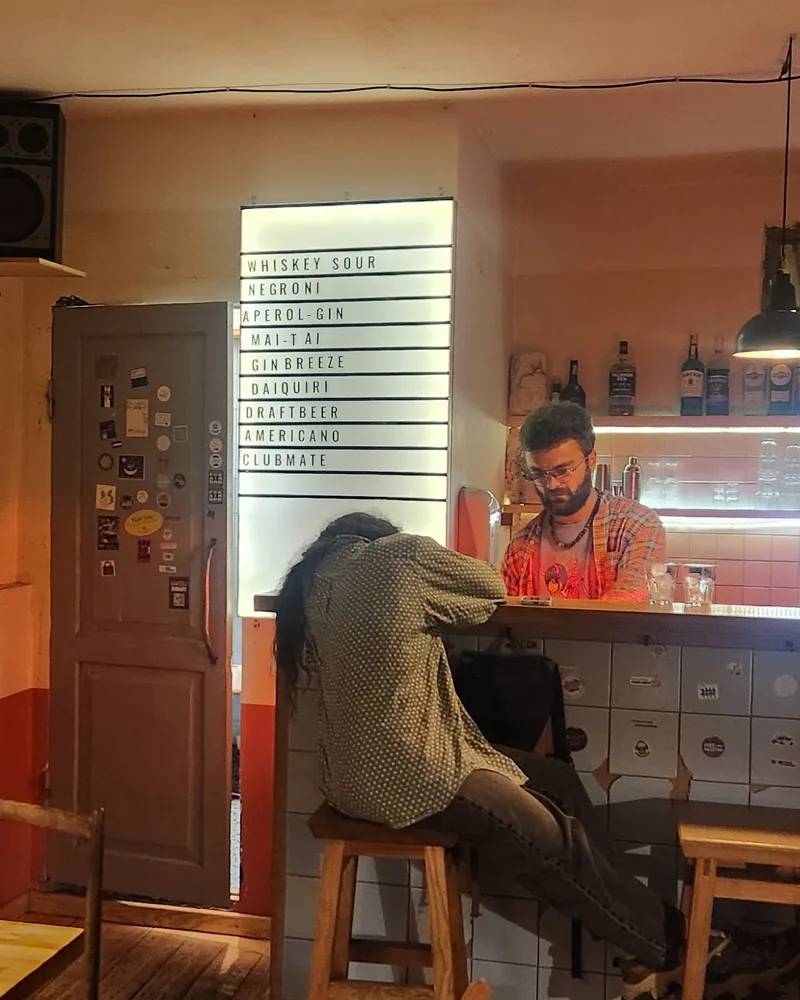 Tiled bar counter with a lit drinks board and shelves of bottles at Muhudo