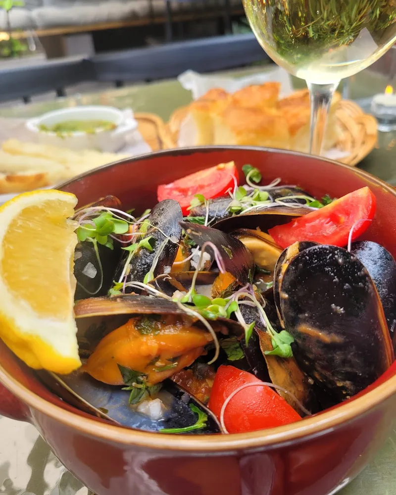 Mussels in a red ceramic bowl with lemon and tomatoes at Mussels Place