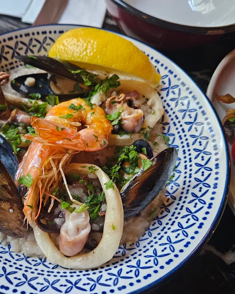 Seafood risotto with shrimp, mussels, and squid in a patterned blue bowl at Mussels Place