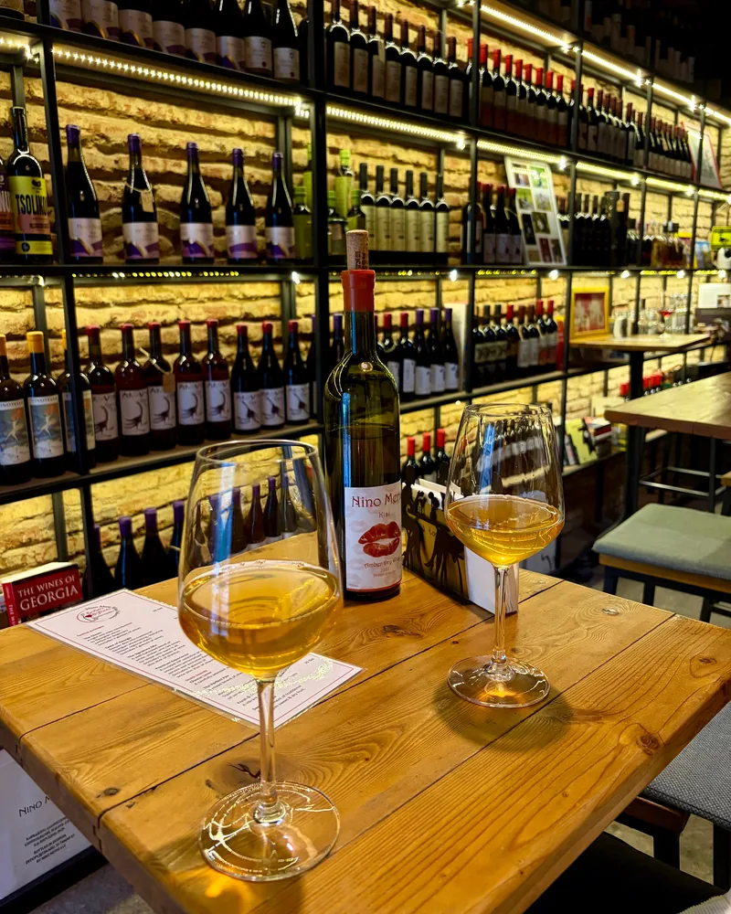 Amber wine in glasses and a bottle on a wooden table at Nino Meris Wine Selection