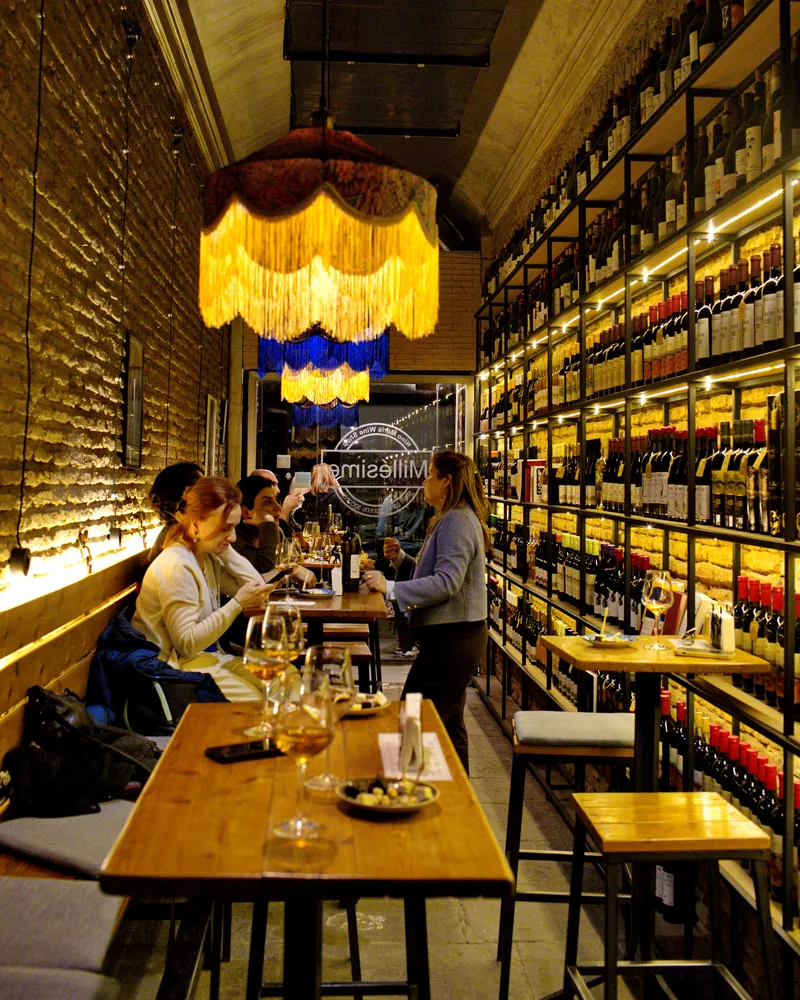 Narrow wine bar with brick wall and floor-to-ceiling wine racks at Nino Meris Wine Selection