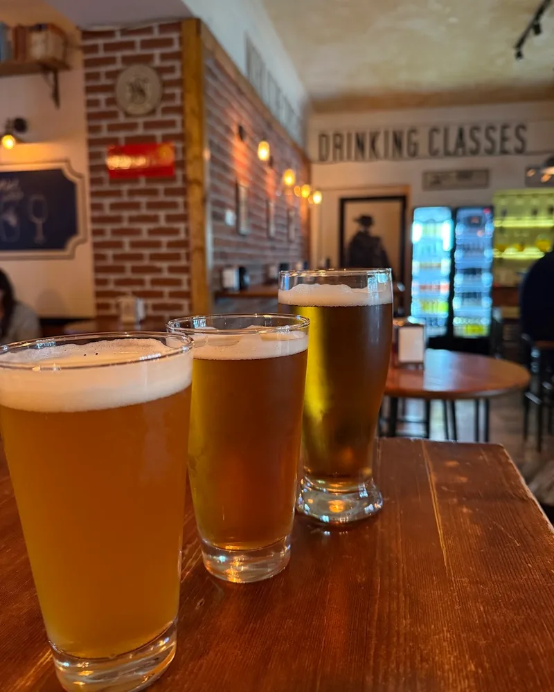 3 glasses of craft beer, from pale gold to amber, on a wooden table in a brick-walled bar