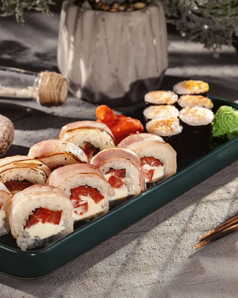 Sushi rolls wrapped in bacon and baked rolls on a dark tray at Oishi Sushi