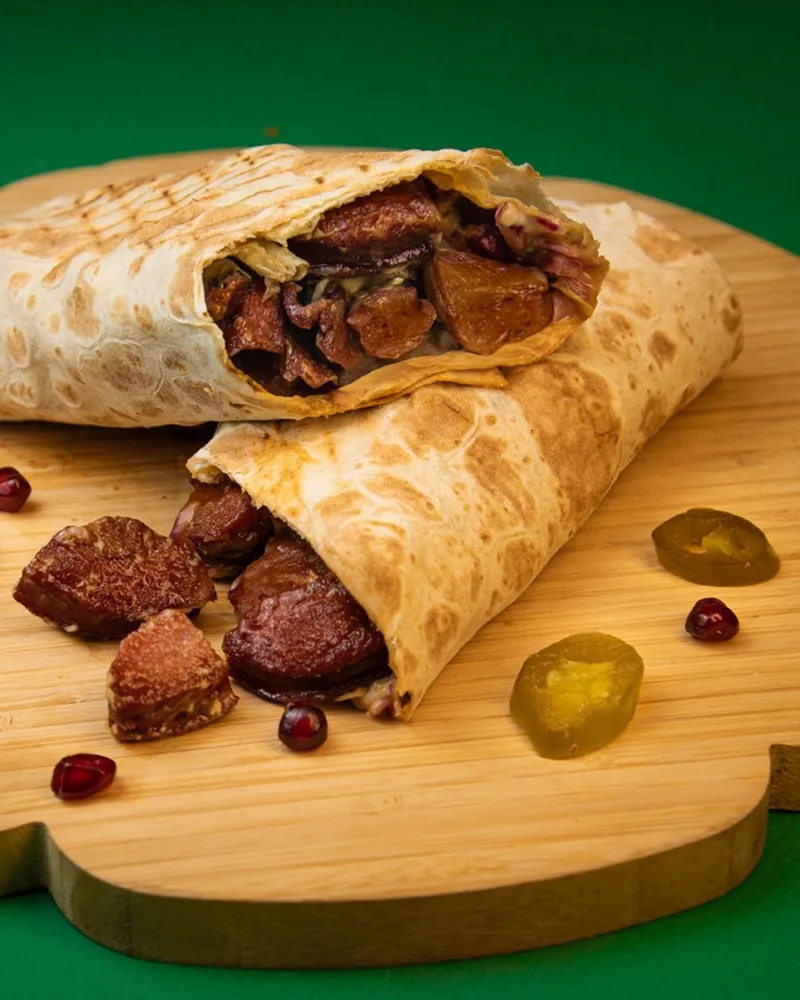 Sliced meat wrap on a wooden board with pickled peppers at OK Shawarma