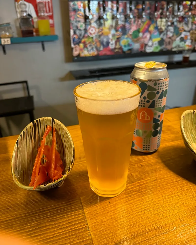 Glass of beer with a craft beer can and a dried fish snack at Optimist Craft Bar