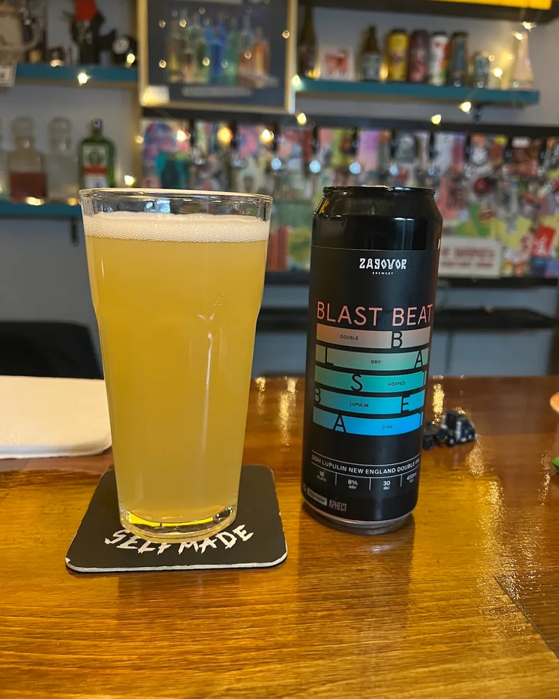 Glass of hazy beer next to a Blast Beat beer can at Optimist Craft Bar