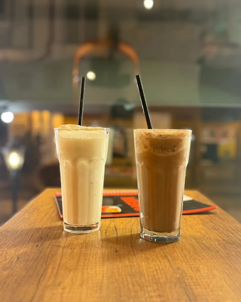 Two iced milkshakes with straws on a wooden table at Orange Café & Karaoke