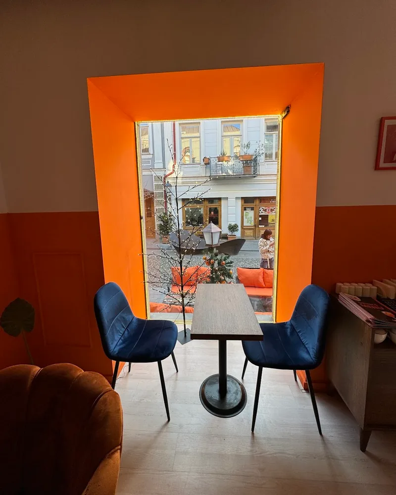 Table and blue chairs by an orange framed window at Orange Café & Karaoke