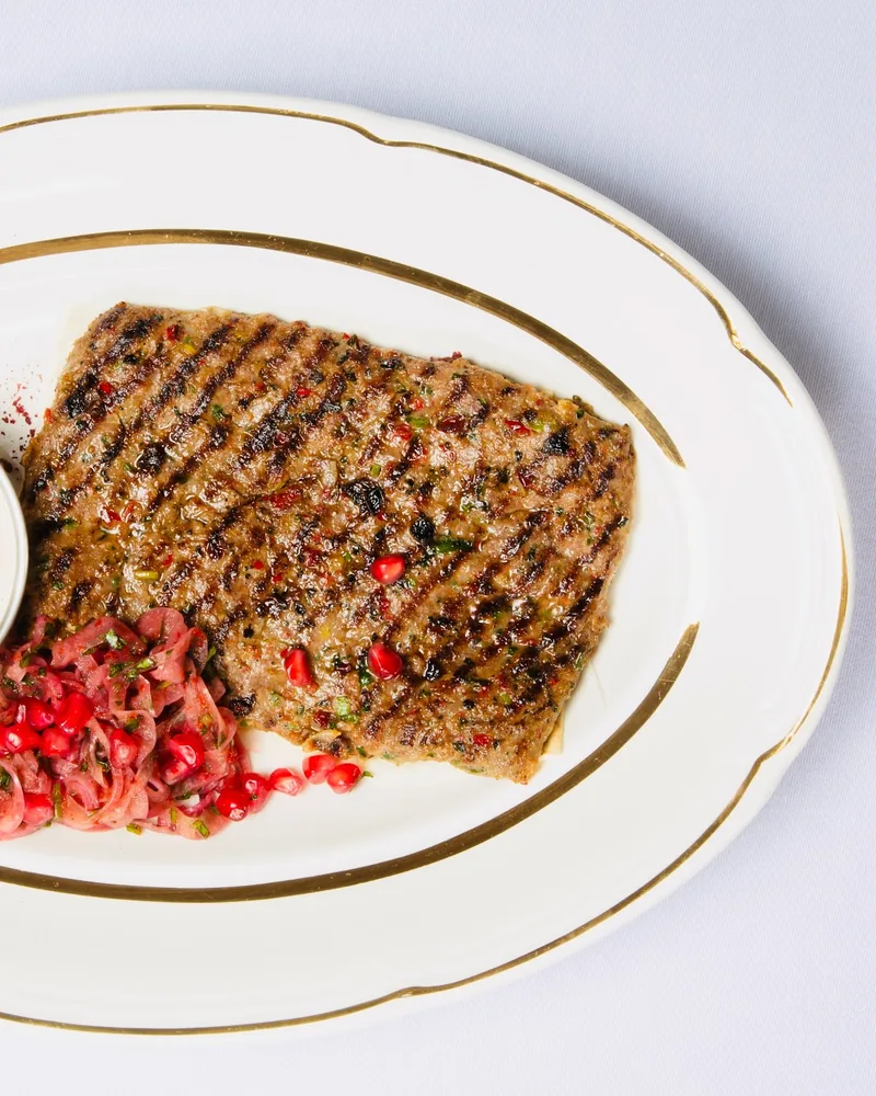 Grilled kebab with dipping sauce and pomegranate salad on an oval platter at OtsY