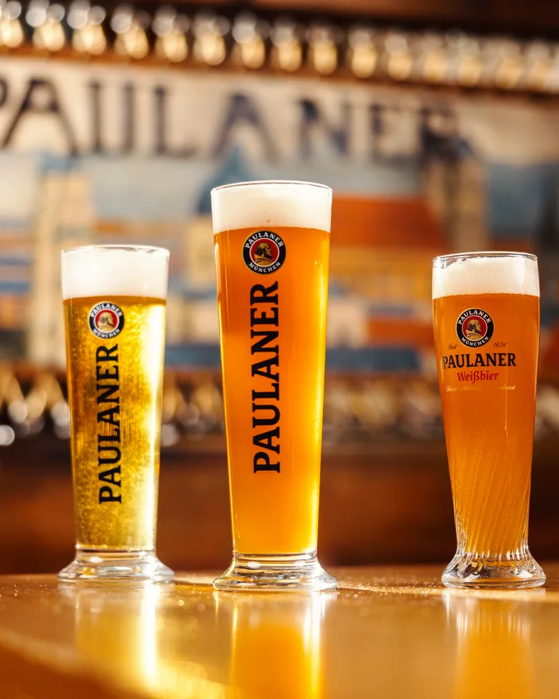 Three glasses of Paulaner beer on a wooden table at Paulaner Beer Garden