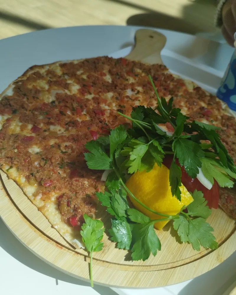Lahmacun served on a wooden board with parsley and lemon at Pide Land