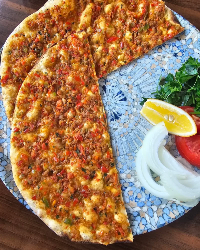 Lahmacun served with lemon, onion and herbs on an ornamental plate at Pide Jimi