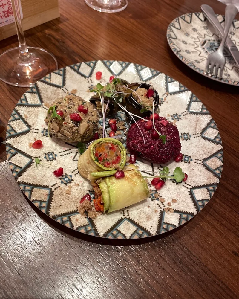 Assorted pkhali on a patterned plate: a round of green pkhali, a round of beetroot pkhali and aubergine rolls, dotted with pomegranate seeds