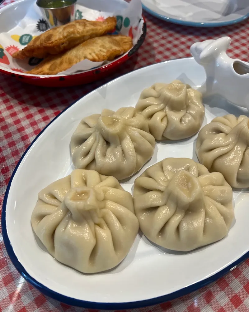 5 pleated khinkali on a white oval plate with a blue rim, with 2 fried pastries in a paper-lined basket behind