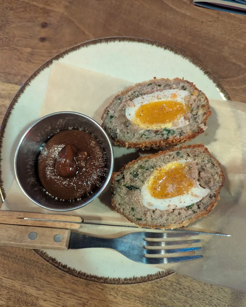 Scotch egg halved on a plate with dipping sauce and cutlery at Pub 44