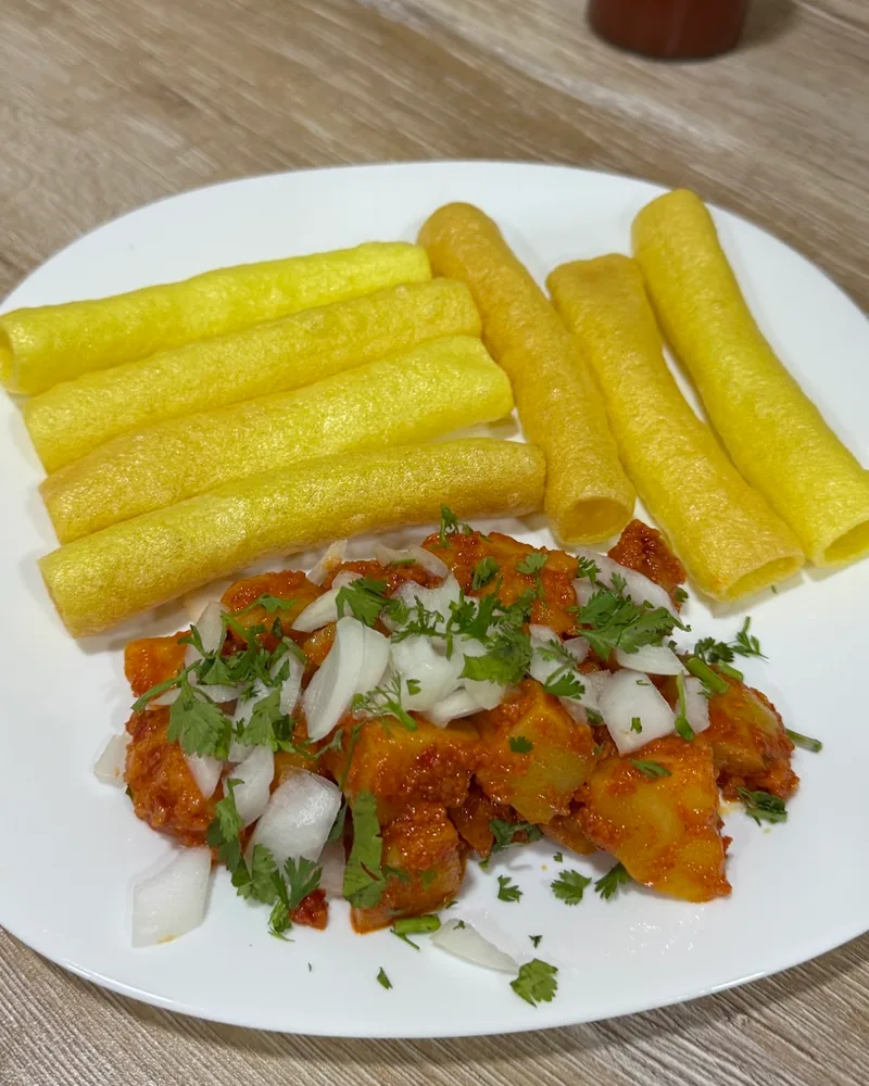 Spicy potato curry garnished with raw onions and coriander, served with fryums at Rasthal