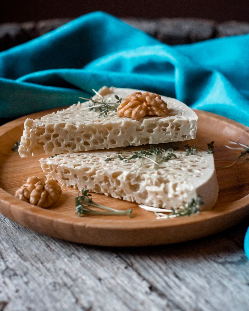 Aerated cheese slices with walnuts and herbs on a wooden plate at Hide