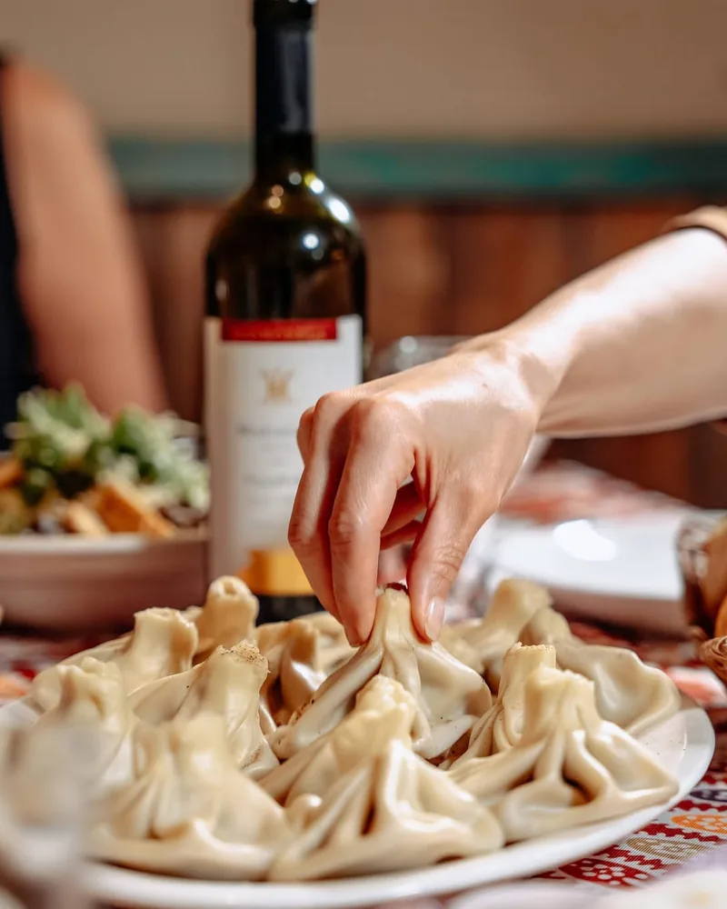Khinkali on a plate being picked up by hand at Pasanauri (Tskneti)