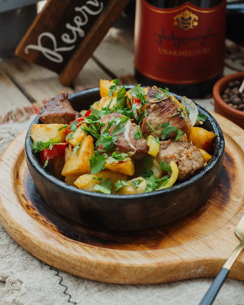 Ojakhuri of pork, fried potatoes and peppers topped with coriander in a black clay dish on a wooden board