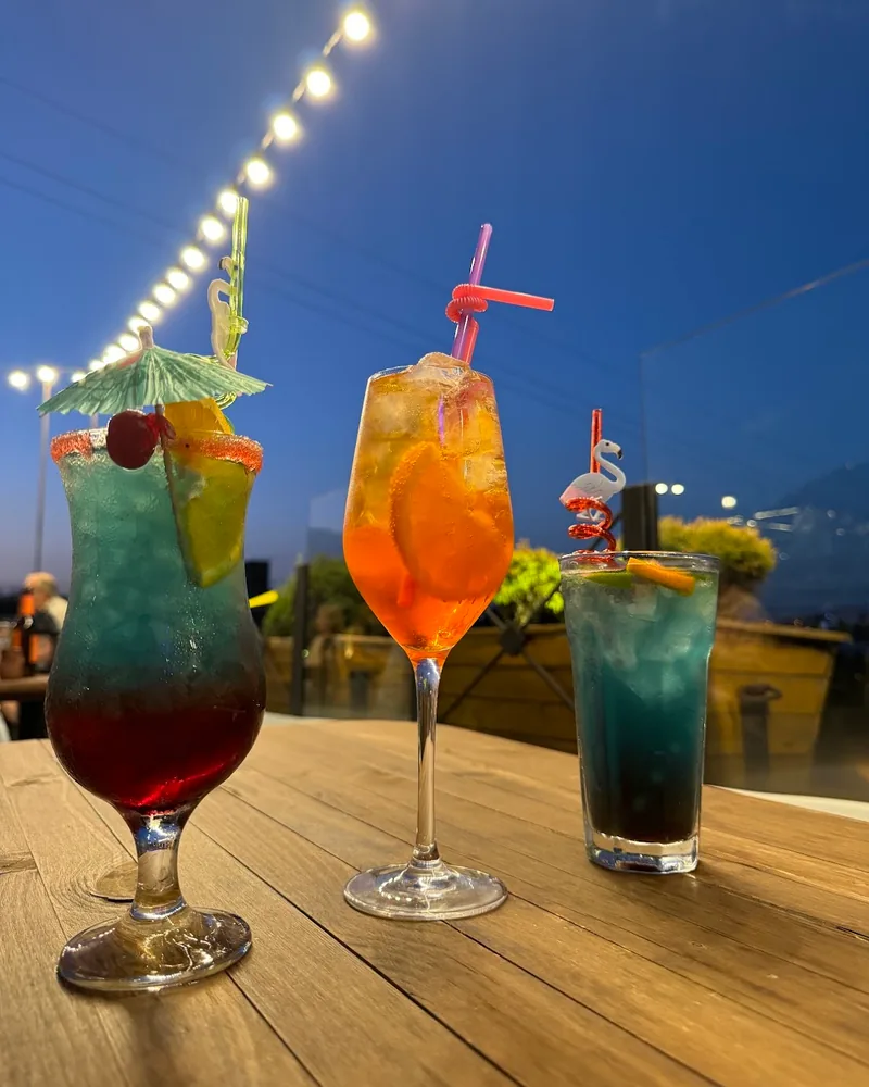 Three colourful cocktails on a wooden table outdoors at Rezidenco Terrace