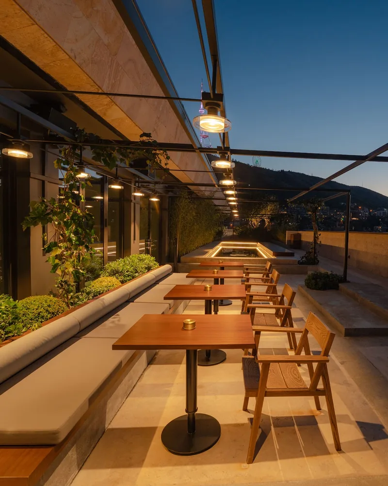 Twilight on the rooftop terrace with wooden tables and banquette seating at Rolling Stone Rooftop Bar