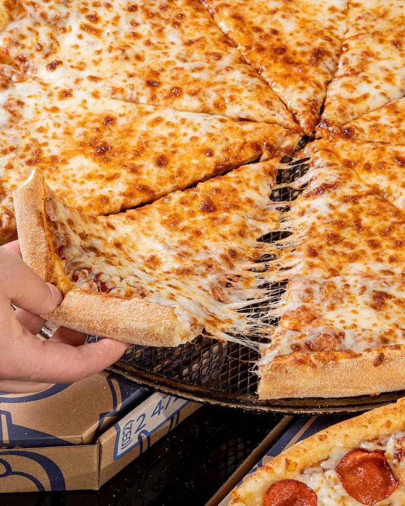 Slice of cheese pizza being pulled from a whole pie at Ronny's Pizza (Dighomi)
