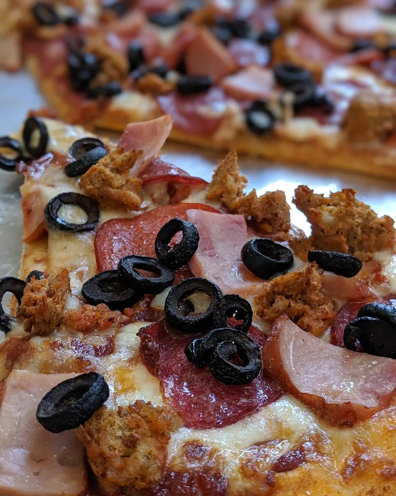 Slice of pizza with ham, sausage, pepperoni, and black olives at Ronny's Pizza (Dighomi)