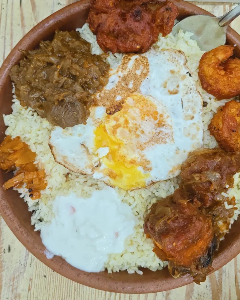 Rice platter with fried egg, curry and prawns in a clay dish at Royal Kitchen in Isani