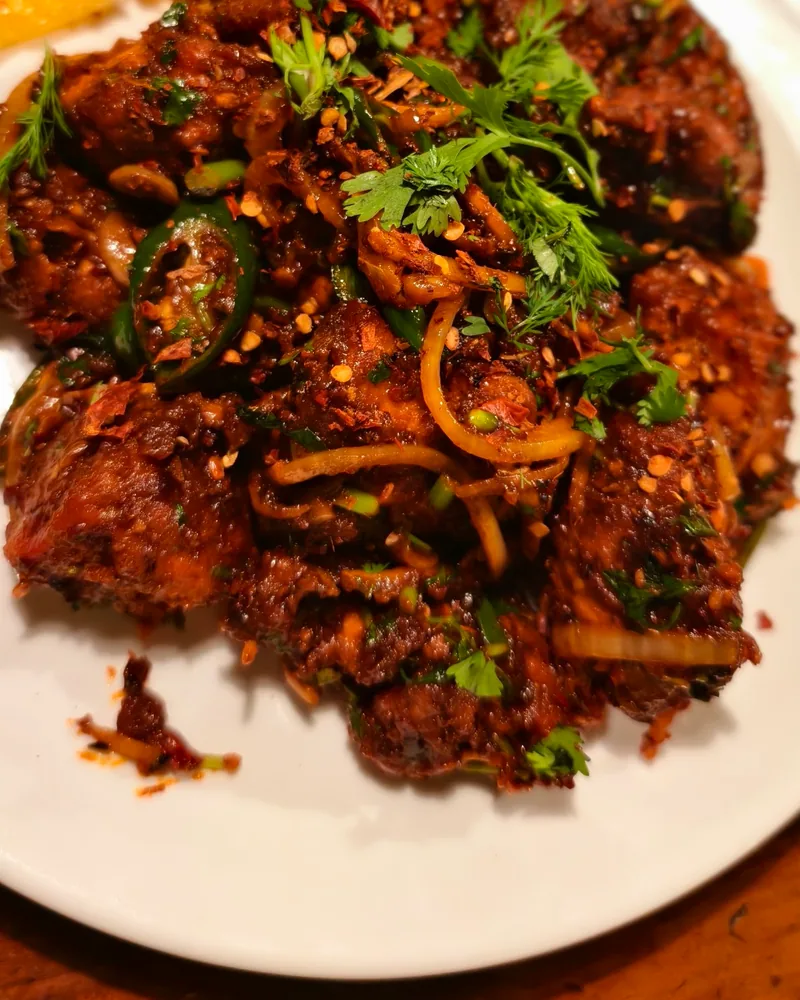 Spicy fried chicken garnished with fresh coriander and orange slices at Royal Kitchen Premium